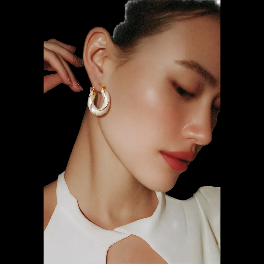 Close-up of a woman wearing gold hoop earrings on a white background.bishop x
