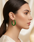Woman wearing a green hoop earring against a neutral background.Bishop X