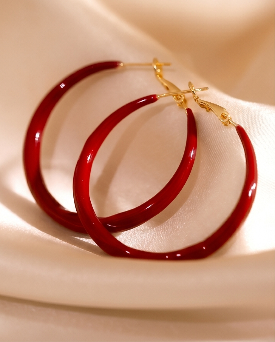 Red hoop earrings with gold clasps on a beige fabric background.bishop x