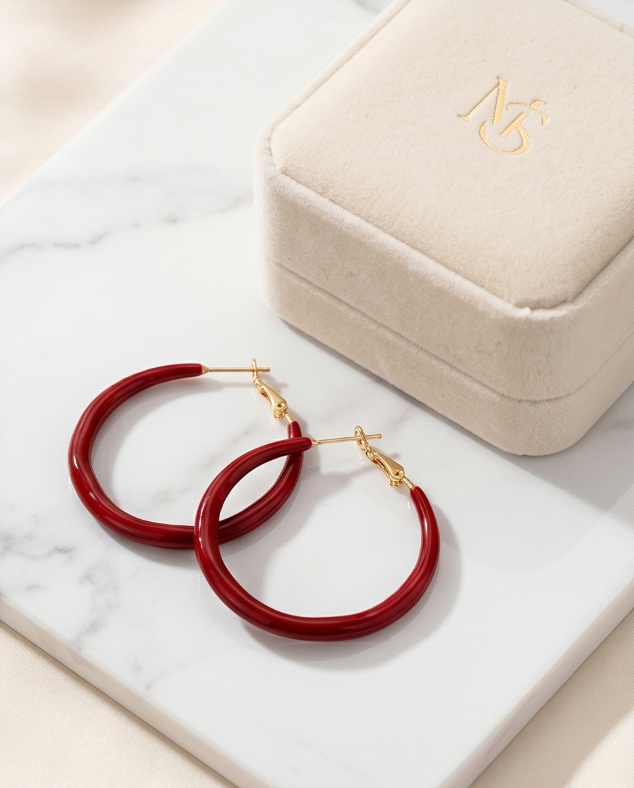 Red hoop earrings with gold accents on a marble surface next to a jewelry box. Bishop X 