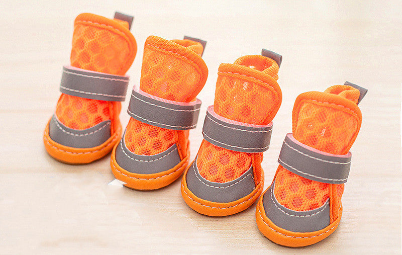 Four orange pet boots with gray straps on a light wooden surface. Bishop X 
