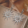 Silver sun-shaped earrings on a wooden surface. Bishop X 