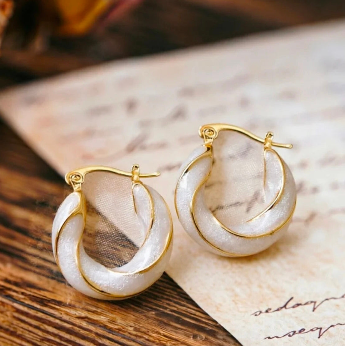 Gold and white hoop earrings on a marble surface with a blurred background.Bishop x