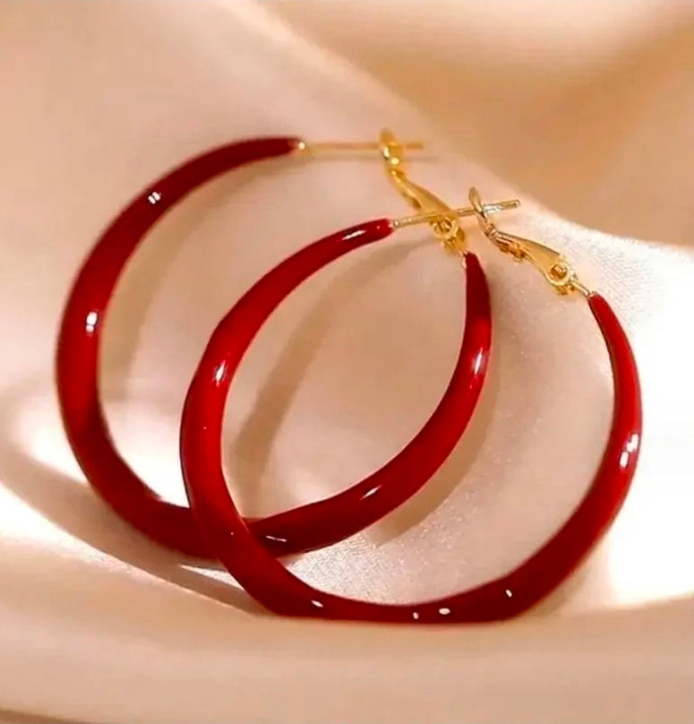 Red hoop earrings with gold clasps on a beige fabric background.bishop X 