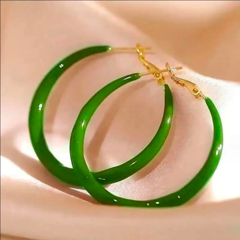 Green hoop earrings with gold accents on a beige fabric background.Bishop X