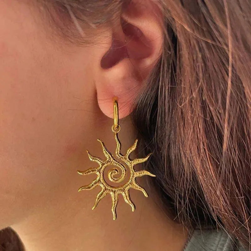 Gold sun-shaped earring worn by a person with brown hair. BISHOP X 