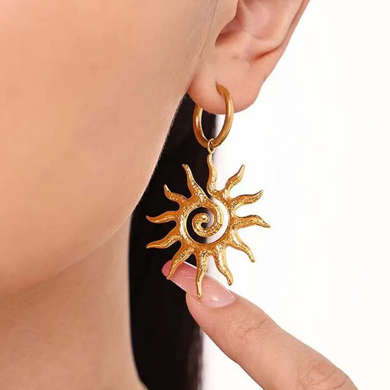 Gold sun-shaped earring worn by a person on a white background. Bishop x 