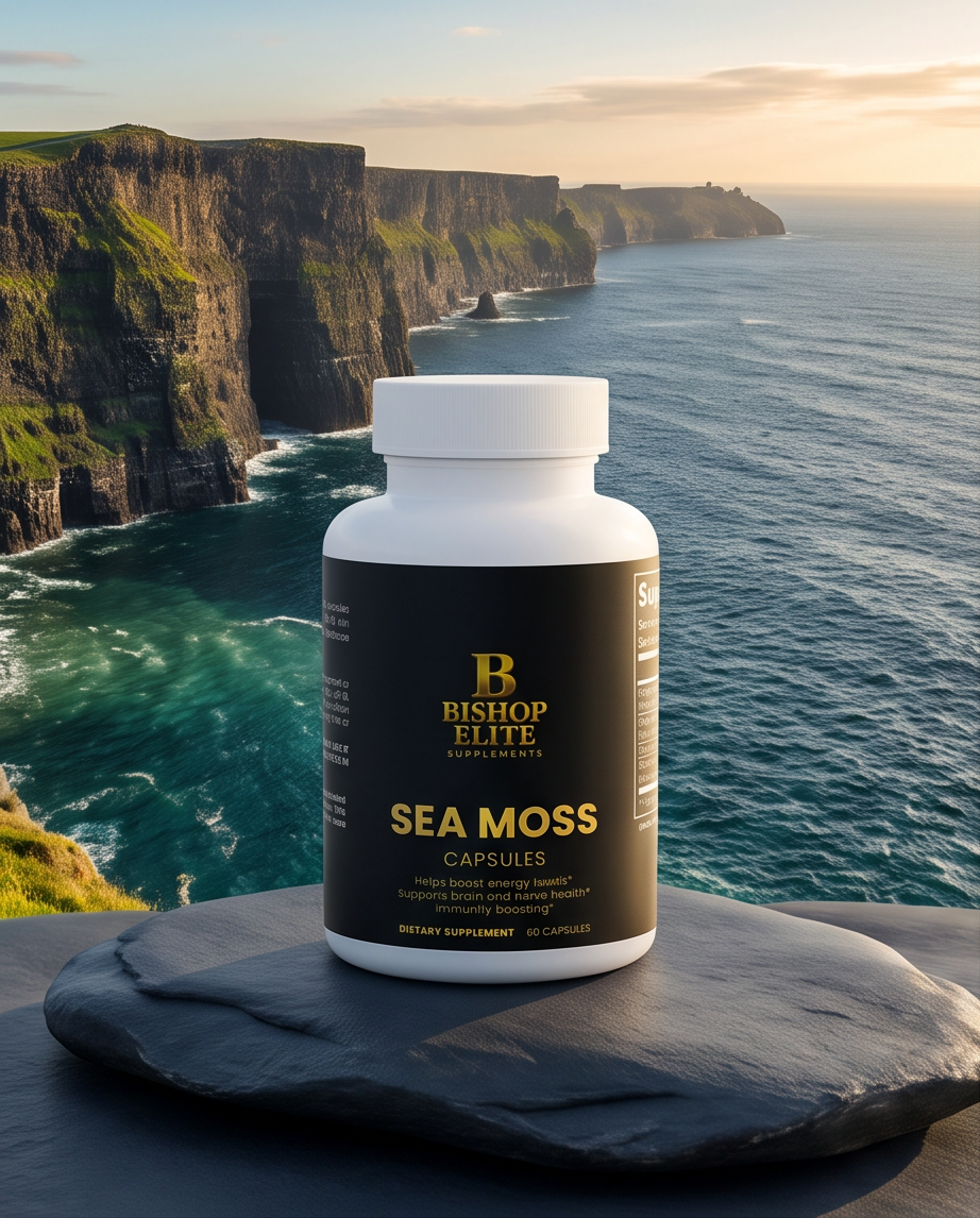 A white bottle of Bishop Elite Sea Moss Capsules with a black label, placed on a dark slate stone with a dramatic coastal cliff and ocean background. Bishop Elite Supplements 