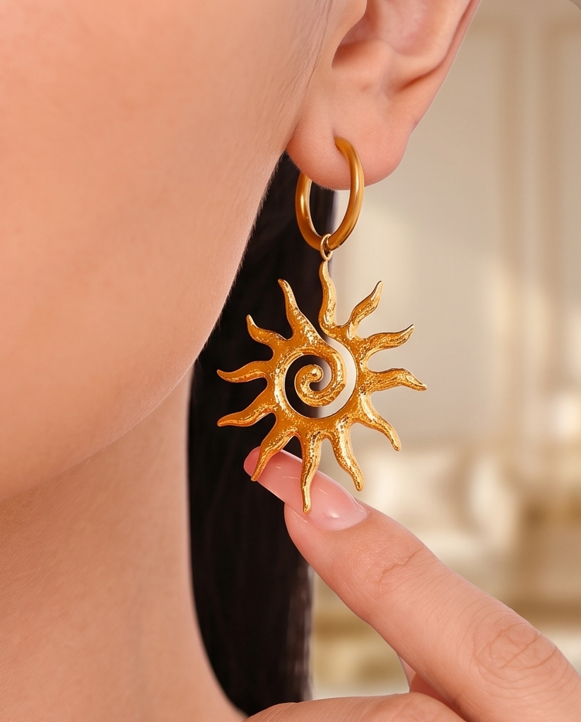 Gold sun-shaped earring being worn on an ear with a blurred background.  Bishop x 
