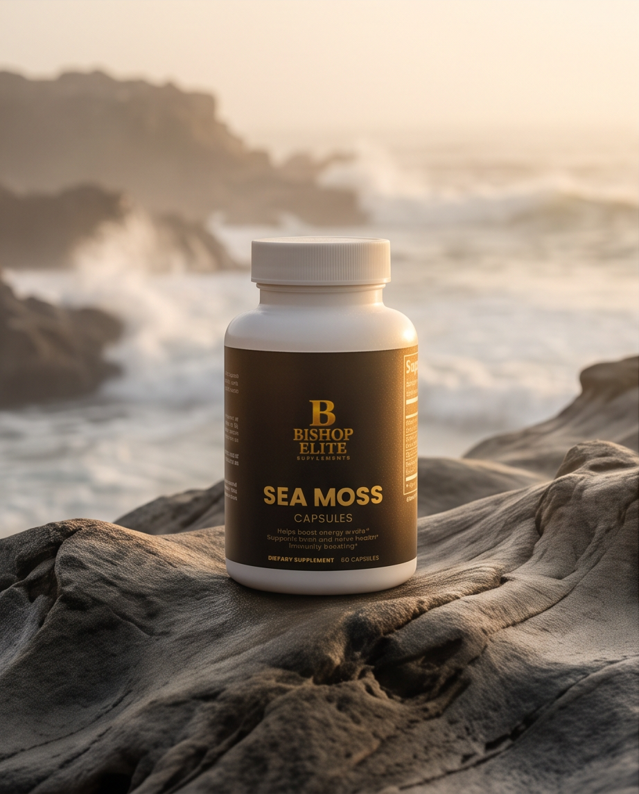 A white bottle of Bishop Elite Sea Moss Capsules standing on a large rock with a blurred ocean and rocky coastline in the background. Bishop Elite Supplements 